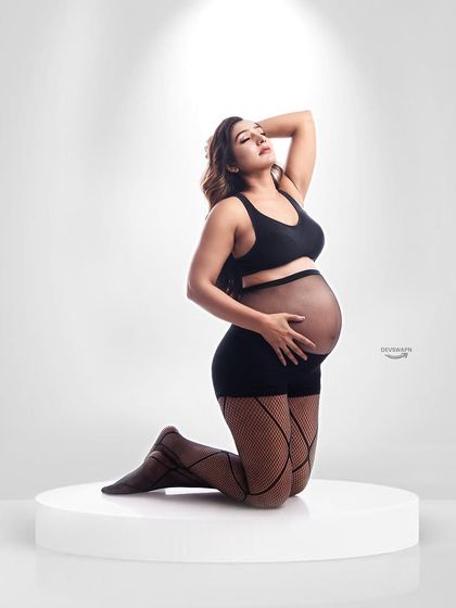 A beautiful and strong pose showcasing a bare bump in a modern, edgy outfit. The spotlight effect adds drama and focus to this contemporary maternity portrait.