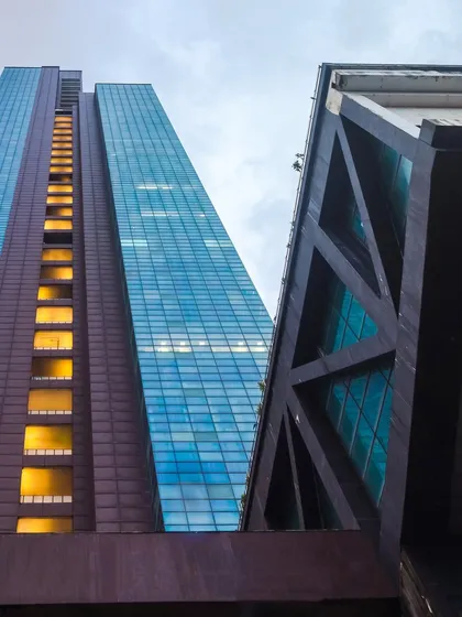 A low-angle view of The Ruby in Dadar, emphasizing its impressive scale and structural design. The exposed truss work and the contrast between the solid podium and the glass curtain wall showcase the technical precision and bold aesthetics of our commercial architecture.