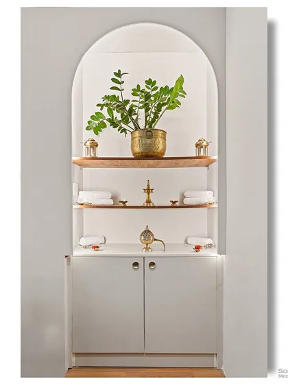 A clean and minimalist storage niche designed for a wellness space. The arched shape, simple white shelves, and brass decor create a sense of calm and order, reflecting a vedic-inspired aesthetic.