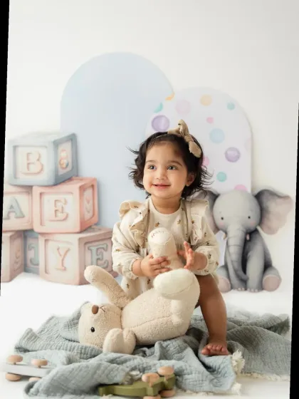 A smiling toddler girl plays with her stuffed bunny during her milestone photoshoot. The soft colors and cute props create a lovely scene.