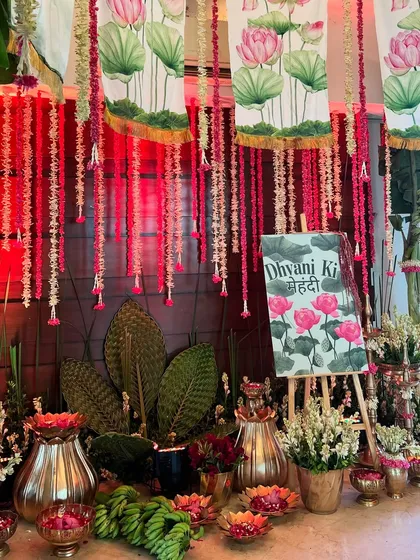 A custom-painted "Dhvani Ki Mehendi" sign, set against a backdrop of Pichwai-inspired lotus paintings and floral strings.