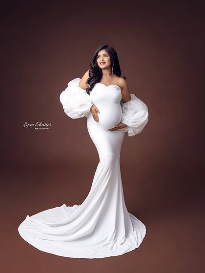 A classic white bodycon gown with dramatic ruffled sleeves, creating a high-fashion maternity look.