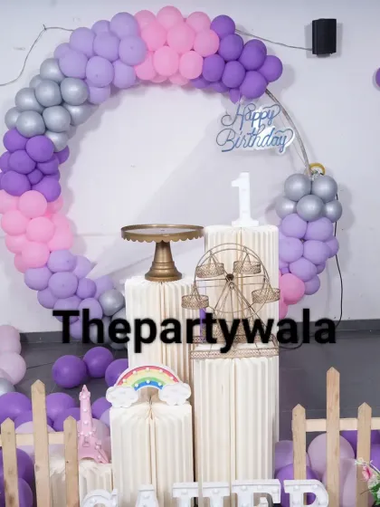 A simple and pretty ring decoration with purple, pink, and silver balloons. The picket fence and rainbow prop add a touch of playful charm.