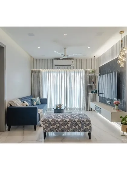 This living room captures my signature style: clean, modern, and comfortable. I used vertical fluted panels and integrated LED lighting to add texture and height to the space, while the floating TV unit keeps the floor clear and creates an airy feel. The pop of blue in the sofa and the geometric ottoman bring personality into the neutral palette.