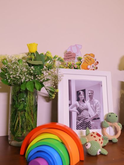 A personal and heartwarming detail at the baby shower. A framed photo of the expectant parents is displayed with a wooden rainbow stacker and handmade crochet turtle toys.
