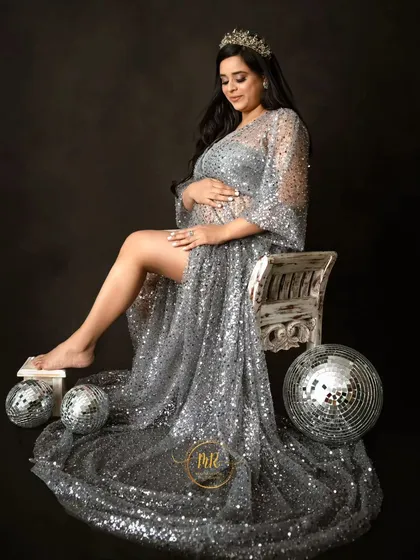 A glamorous seated portrait in a sequined silver gown. The mother-to-be is surrounded by disco ball props, adding a fun and celebratory feel to the shoot.