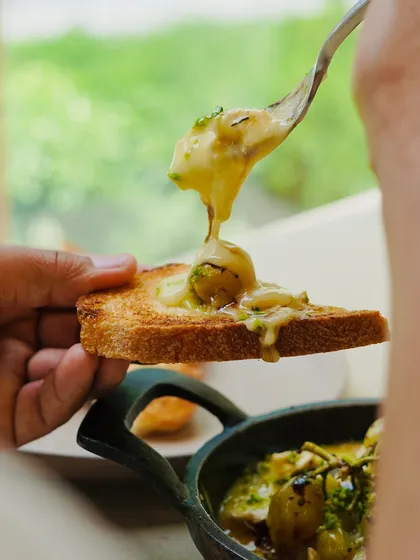 This is what happens when incredible local ingredients come together. We take artisanal brie, melt it until bubbly with farm-grown herbs, and top it with oven-blistered Kumaoni grapes. It's a truly unique appetizer, perfect for sharing over sourdough toast.
