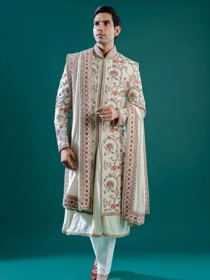 An off-white sherwani featuring exquisite, multi-colored floral embroidery that cascades down the front and sleeves. This piece, complete with a matching stole, is a wearable work of art for a day wedding.