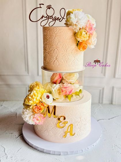 This engagement cake features a unique floating design with a flower-filled separator. The textured tiers are personalized with the couple's initials, creating a modern and romantic centerpiece.