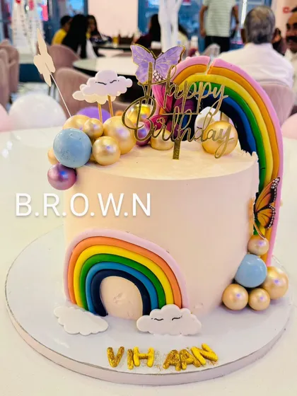 A beautiful rainbow and butterfly themed cake. The design features two fondant rainbows, shimmery gold and blue spheres, and delicate butterflies.
