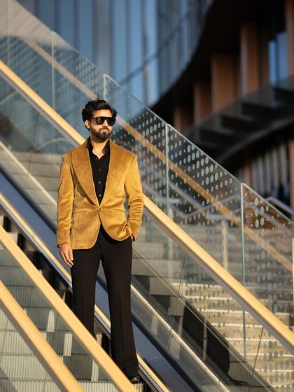 The mustard velvet blazer, viewed from a low angle, emphasizes its strong shoulder line and tailored fit.