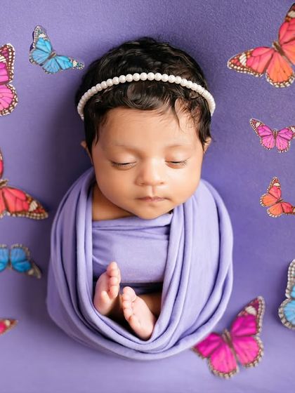 A newborn wrapped in a lavender swaddle, surrounded by colorful butterflies. This whimsical setup creates a dreamy, magical portrait.