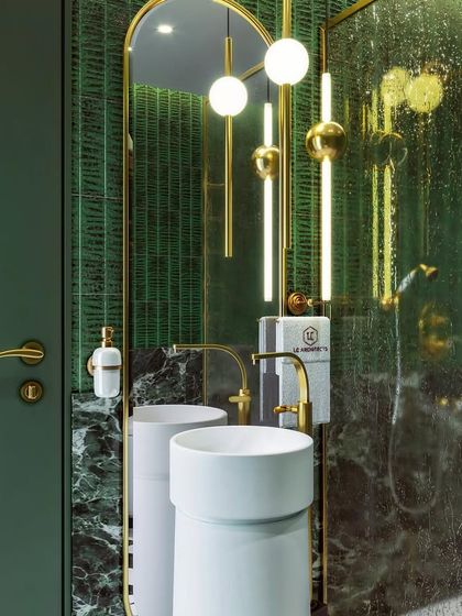 A master bathroom designed to be a sanctuary. This concept in green and gold features pedestal sinks, unique pendant lighting, and a mix of dark marble and textured green tiles.