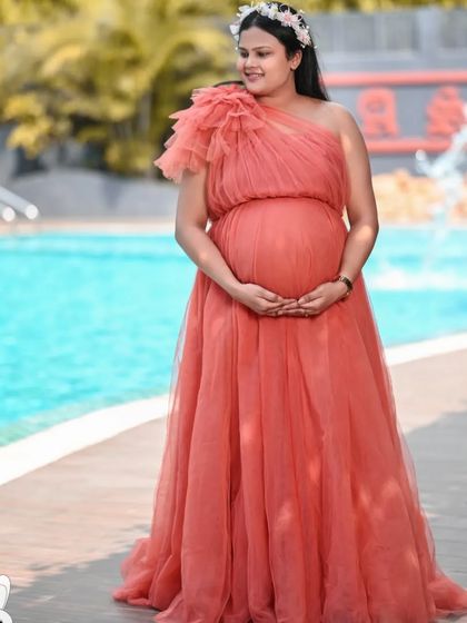 A solo portrait of a client by the pool in a one-shoulder coral-pink tulle gown. The color is soft and flattering, and the style is both elegant and comfortable.
