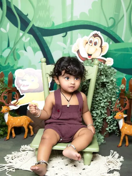 Sitting like a king or queen of the jungle in a green chair, this baby is surrounded by friendly animal props in a lush green backdrop.