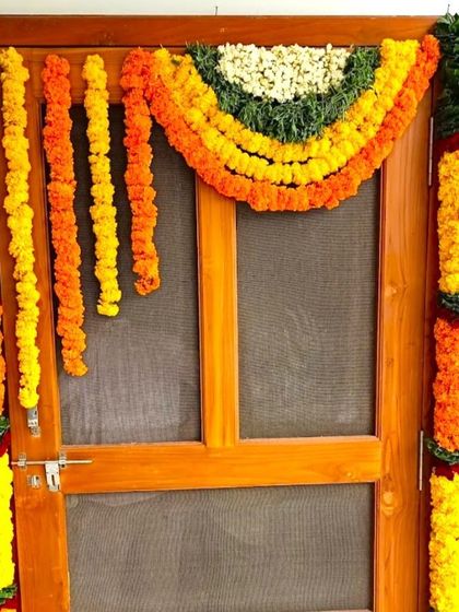 A housewarming flower decoration for an apartment door with a screen. The door is framed with garlands of orange and yellow marigolds.