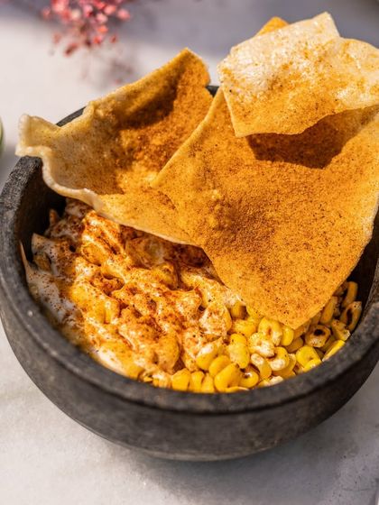 Esquite, the perfect start to your meal. It features charred corn kernels, confit garlic aioli, and fresh cilantro, served with crispy tortilla chips.