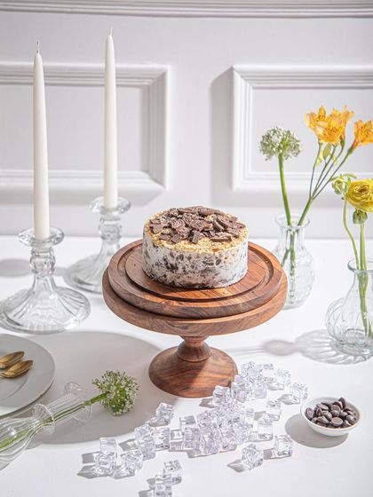 A Cookies and Cream ice cream cake on a wooden stand, surrounded by fresh flowers and candles, creating an atmosphere of simple elegance.