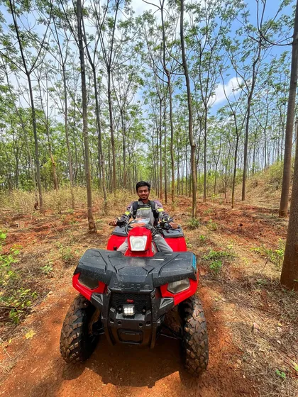 A solo rider pauses on his red Polaris ATV in the middle of a beautiful forest trail. The tall, slender trees create a natural tunnel, making for a peaceful and picturesque moment.