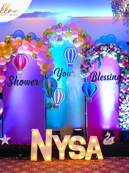A vibrant birthday party setup for "Nysa". The decor features a hot air balloon theme, colorful balloon arches, and large, illuminated letters spelling out the name.