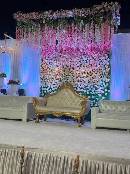A beautiful stage setup featuring a wall of ombre flowers transitioning from pink to white. The hanging wisteria and classic gold-and-white sofa add a touch of romance and elegance.