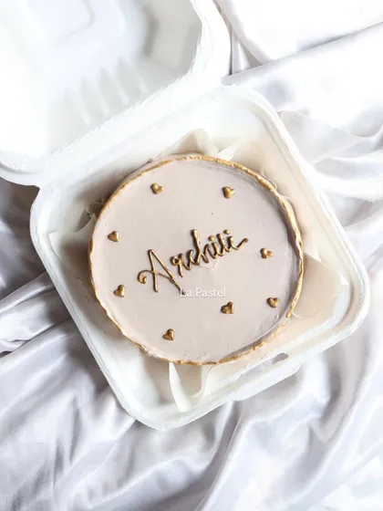 A simple and elegant bento cake with a custom name in gold script, surrounded by tiny hearts. Perfect for a minimalist celebration.