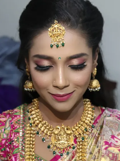 A close-up of a South Indian bride's makeup. The focus is on the shimmery pink and gold eye makeup, which adds a touch of modern glam to the traditional look, paired with temple jewellery and a pink silk saree.
