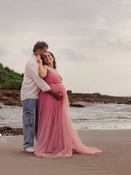 An embrace on the shoreline. This wide shot captures the couple in the beautiful coastal landscape, creating a stunning and epic maternity portrait.