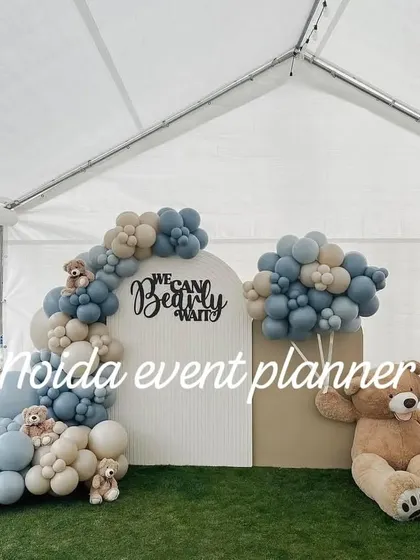 A 'We Can Bearly Wait' baby shower setup inside a tent, using muted blue and beige balloons and wooden 'BABY' blocks for a clean, modern look.