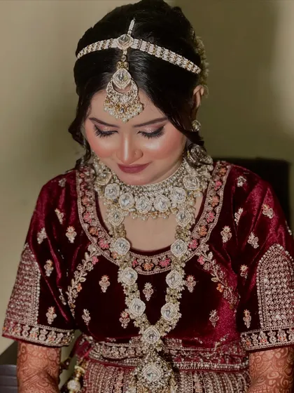 This bride opted for a beautiful maroon velvet outfit with stunning silver-toned jewellery. The makeup features soft, shimmery eyes and a complementary lip color.