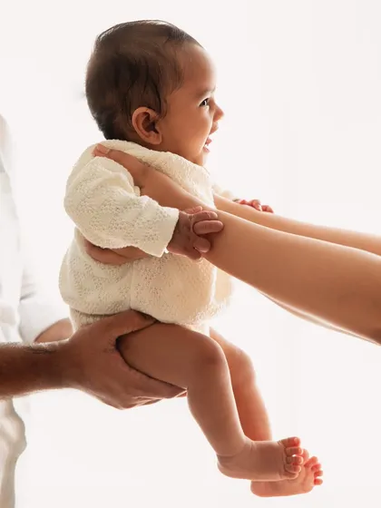 A beautiful silhouette showing a baby being passed between parents. This artistic shot highlights the trust and connection within the family during a 6-month session.