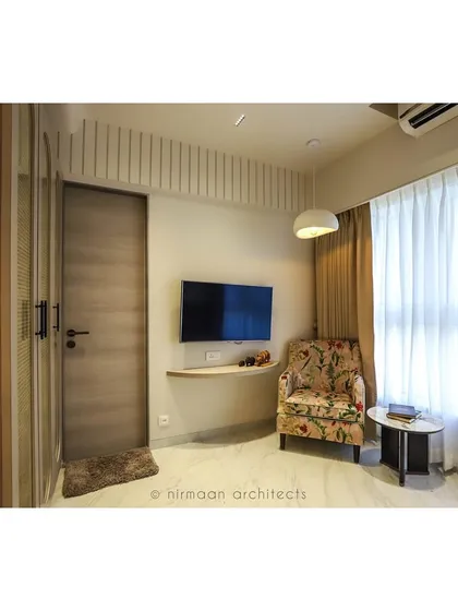 A full view of the guest bedroom, showing the comfortable armchair, floating TV shelf, and ample natural light. We design guest rooms to be as welcoming and comfortable as the rest of the home.