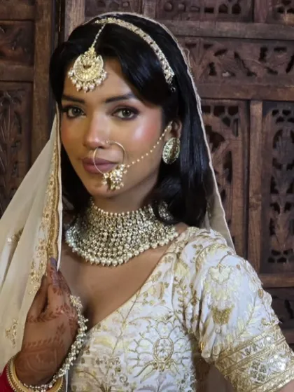An elegant bride in a white and gold lehenga, wearing a simple but beautiful pearl choker set. This is a great choice for a minimalist bride.