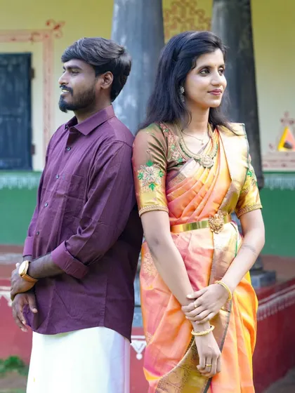A classic back-to-back pose in front of a traditional house. The bride's orange and pink saree with an embroidered blouse is a highlight.