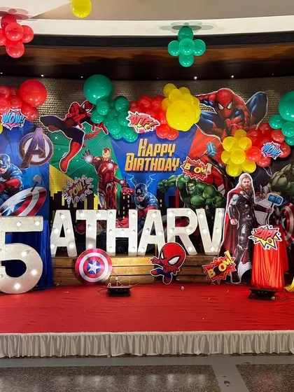 I go all out with action-packed themes for kids. This Marvel Avengers birthday stage is filled with life-sized cutouts of superheroes like the Hulk and Iron Man, a dynamic backdrop, marquee letters, and colorful balloon clusters.