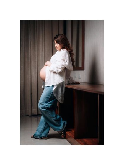 A relaxed and stylish studio portrait of a mom-to-be in flared jeans and an open white shirt, showcasing her bare bump. This look is both casual and beautifully intimate.