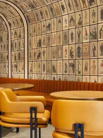 This office cafeteria features a barrel-vaulted ceiling covered in vintage-style wallpaper, paired with warm leather banquettes. The design creates a cozy, club-like atmosphere that feels distinct from the workspace.