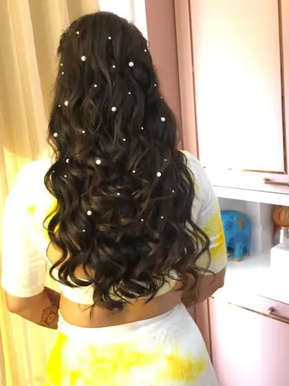 A back view of a half-up hairstyle with soft waves, adorned with scattered pearls. This is a delicate and romantic look, perfect for a Haldi or Mehendi ceremony.