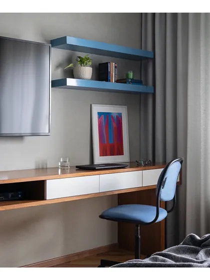 A functional and stylish home office nook within a bedroom. The blue floating shelves add a touch of color, while the wooden desk provides a warm, dedicated workspace without cluttering the room.