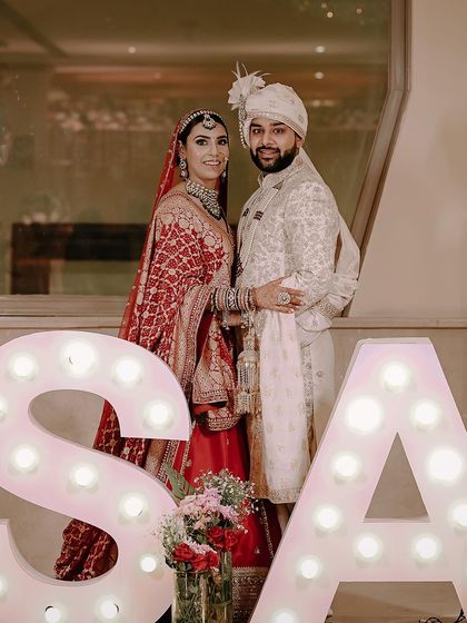 A fun wedding portrait with the couple's initials in large, lit-up letters. This kind of personalized detail makes for a unique and memorable wedding photo.