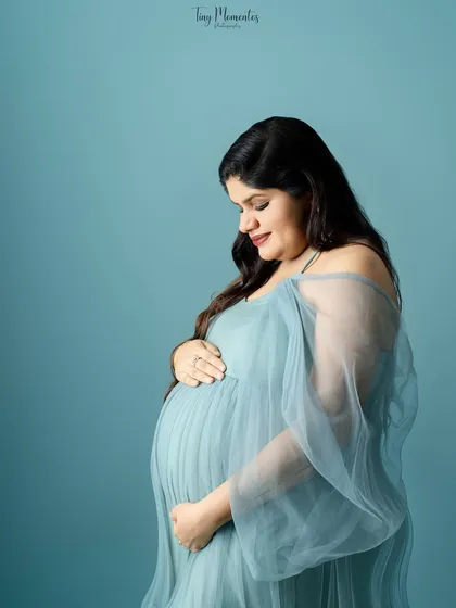 A gentle close-up in the beautiful blue gown, focusing on the mother's serene expression as she cradles her bump.