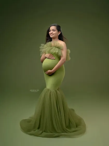 A simple, elegant full-length portrait against a solid olive green background. This classic shot puts all the focus on you, your baby bump, and the beautiful flow of the gown.