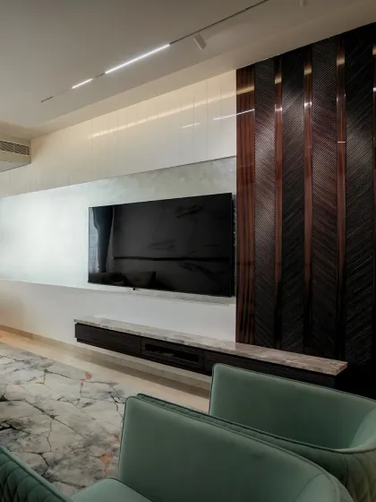 This media wall combines functionality with high-end finishes. A floating marble-topped console sits below the screen, complemented by a rich, chevron-patterned wood panel that adds texture and visual interest to the minimalist space.