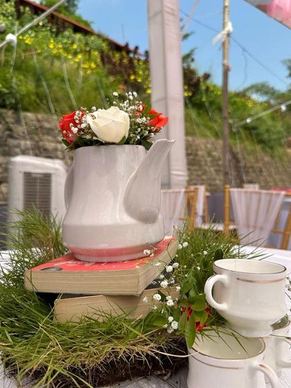 A creative centerpiece for a themed event, featuring a vintage-style teapot used as a vase, placed on a stack of old books.