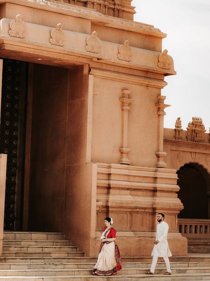 The couple descends the steps of a majestic heritage building. This wide shot captures the scale of the architecture and the grace of their traditional attire in a candid moment.