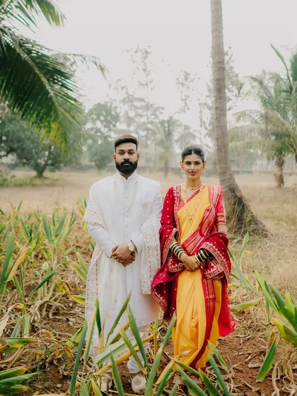 A formal yet beautiful portrait of the couple standing together amidst nature. This image showcases the grandeur of their traditional outfits and their strong presence as a couple.