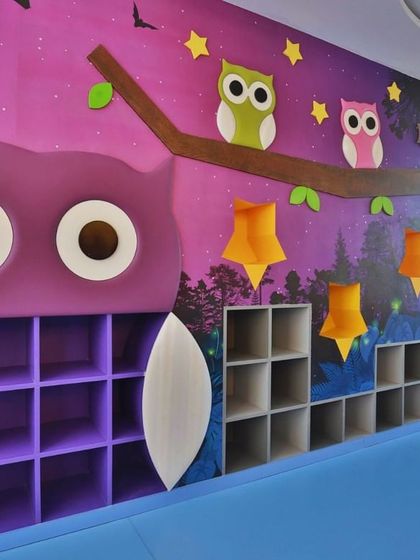 A nocturnal forest-themed room with a large owl-shaped bookshelf and star-shaped lights. The design uses a darker, calming palette to create a cozy and magical atmosphere for storytelling and quiet activities.