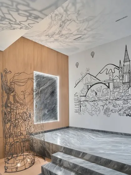 The 'Moving Cache' metal sculpture is paired with a monochrome line-art mural, creating a multi-layered memory reel of the family's travels. The metalwork appears to emerge directly from the wall illustration.