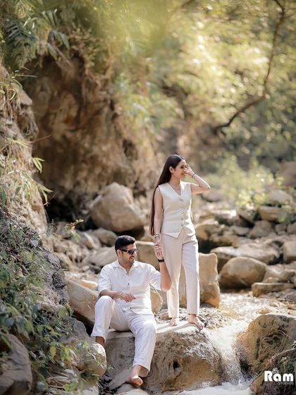 A pre-wedding shoot set against a natural waterfall in Rishikesh. The couple's coordinated white outfits stand out beautifully against the lush greenery and rocks, creating a fresh and adventurous feel.
