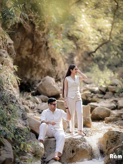 A pre-wedding shoot set against a natural waterfall in Rishikesh. The couple's coordinated white outfits stand out beautifully against the lush greenery and rocks, creating a fresh and adventurous feel.